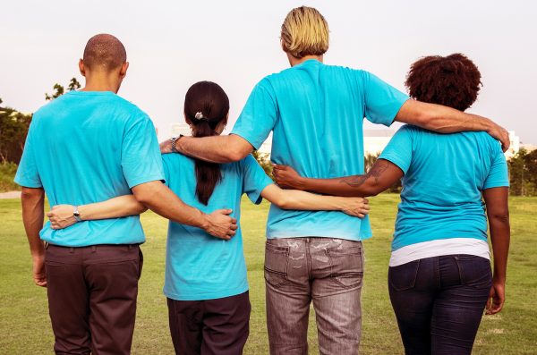 four diverse men and women stand with their backs to the camera with their arms wrapped around each other in solidarity