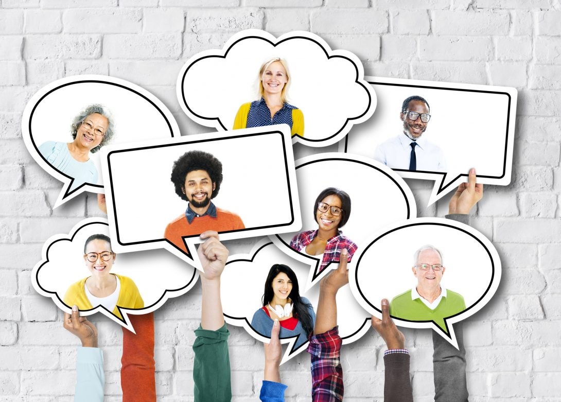 hands hold up cutout speech bubbles containing the faces of a diverse group of men and women