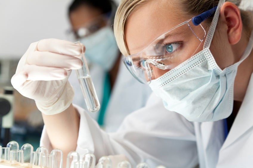 researcher with mask and goggles looking at test tube