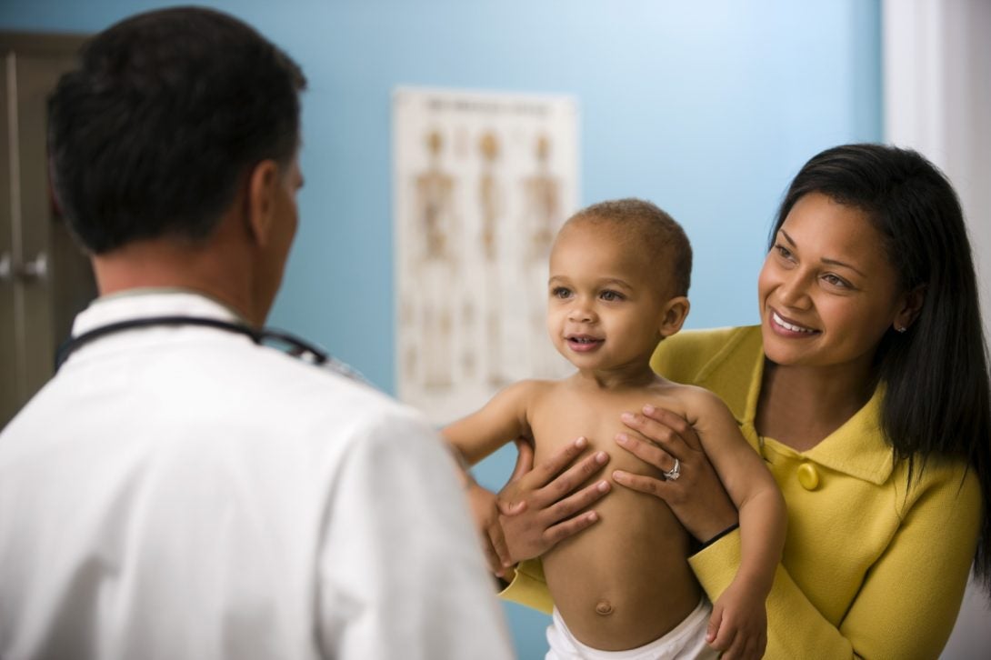 a smiling mother holds her baby up for a doctor to see