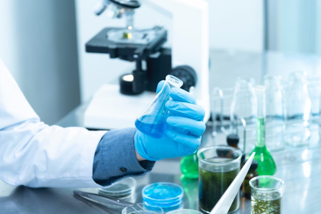 a gloved hand in a white lab coat holds a beaker full of liquid