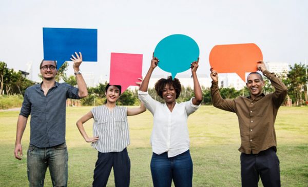 a diverse group of men and women hold up speech bubble cutouts