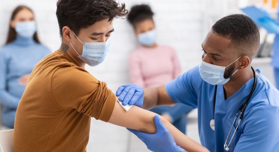 a man wipes an injection site for a male vaccine patient