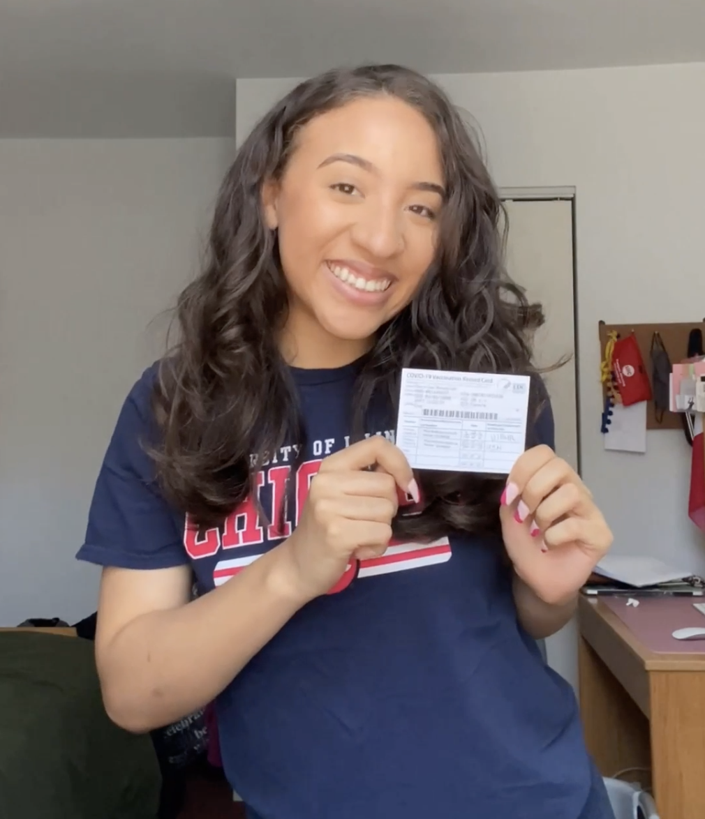 a smiling UIC student holds her vaccination card
