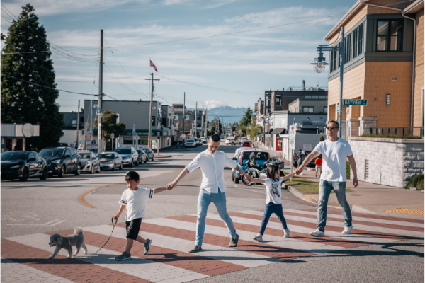 two children, two adults and a dog hold hands while crossing a neighborhood street