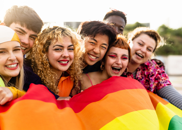 a group of young LGBTQ people celebrate pride month with a rainbow flag