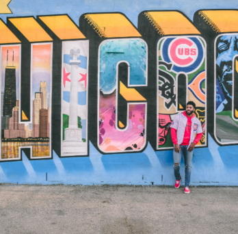 man in a cubs jersey stands in front of a Chicago city mural 