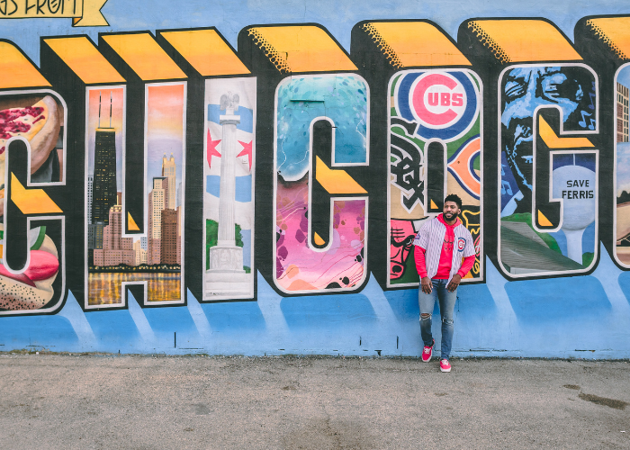man in a cubs jersey stands in front of a Chicago city mural