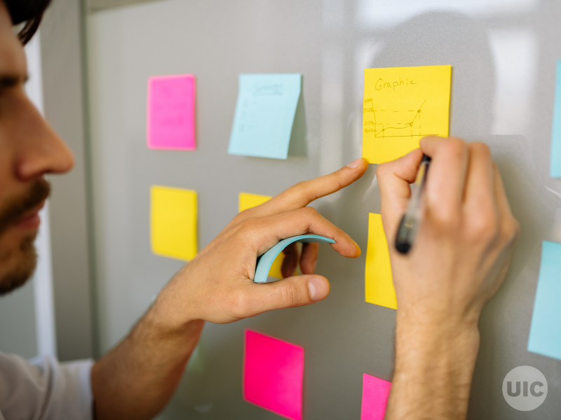 A man writes on a board full of sticky notes