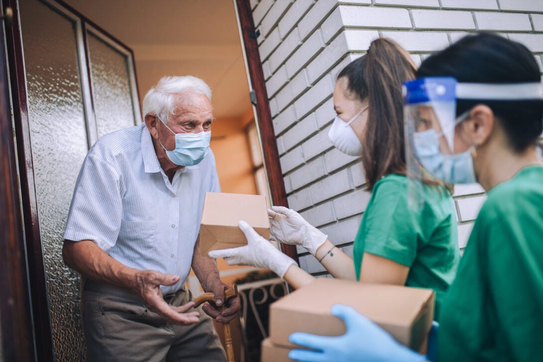 Healthworkers distribute supplies to an elderly man wearing a surgical mask