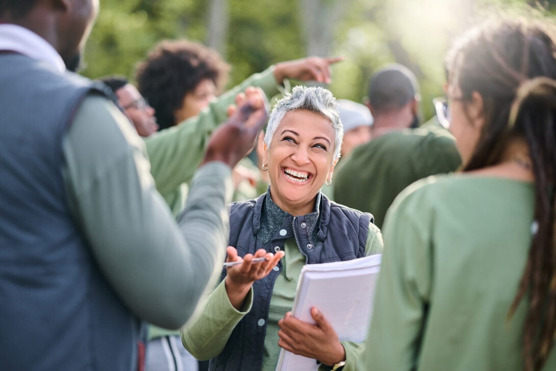 a woman holding a notepad smiles at community members during an event