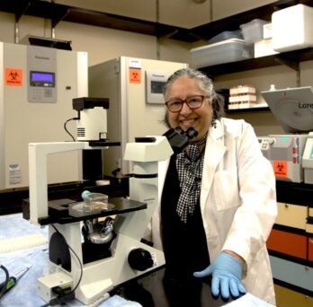 Dr. Neelu Puri smiles from behind a microscope in her laboratory 