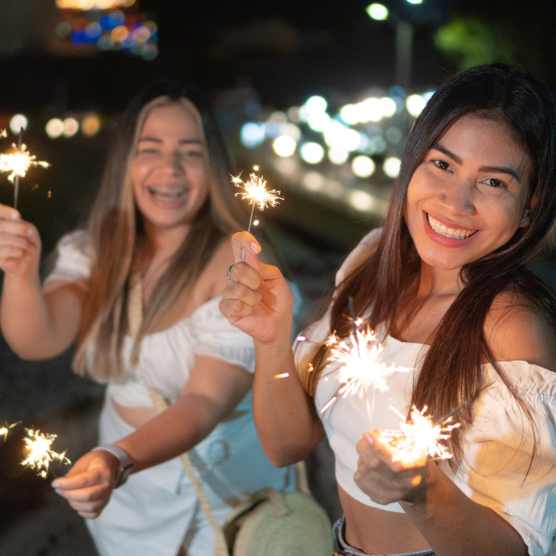 two teen girls hold sparklers and smile at the camera